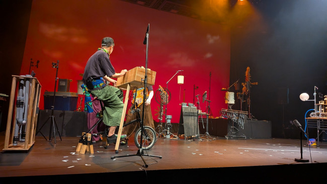 赤い照明の舞台で創作楽器を演奏するSOUDA「音楽の島」